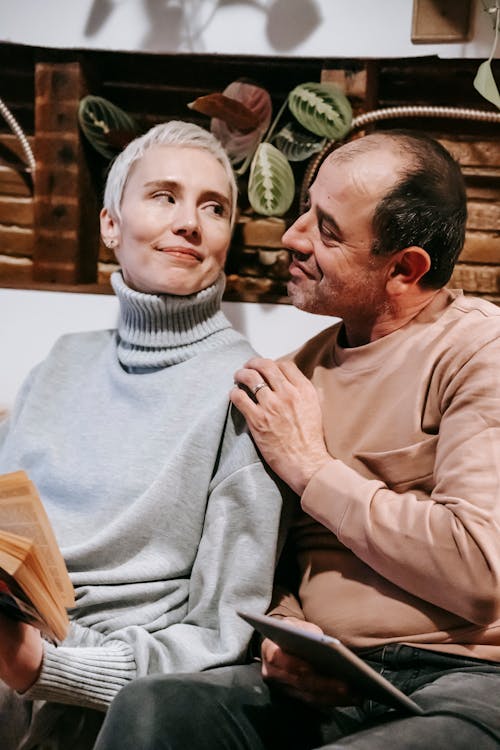 Content diverse couple with book and tablet in hands looking at each other happily