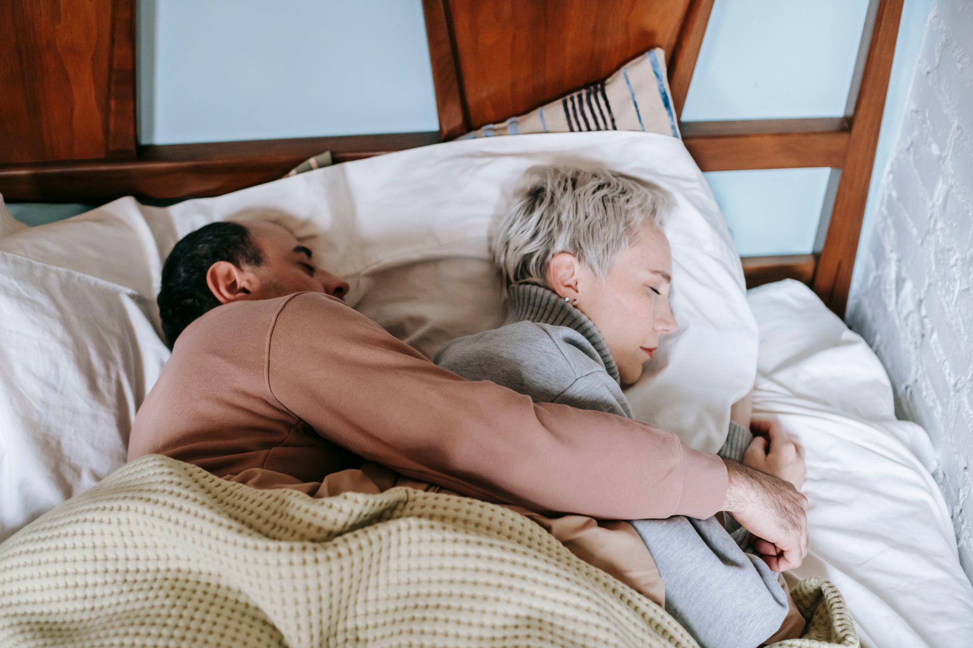 From above of middle aged ethnic man in casual clothes lying on bed and embracing wife while sleeping together on comfortable bed in sunny morning
