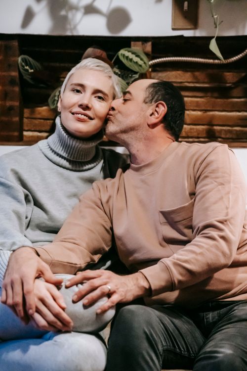 Free Loving ethnic middle aged male in casual clothes kissing cheek of happy wife while resting together on sofa at home Stock Photo