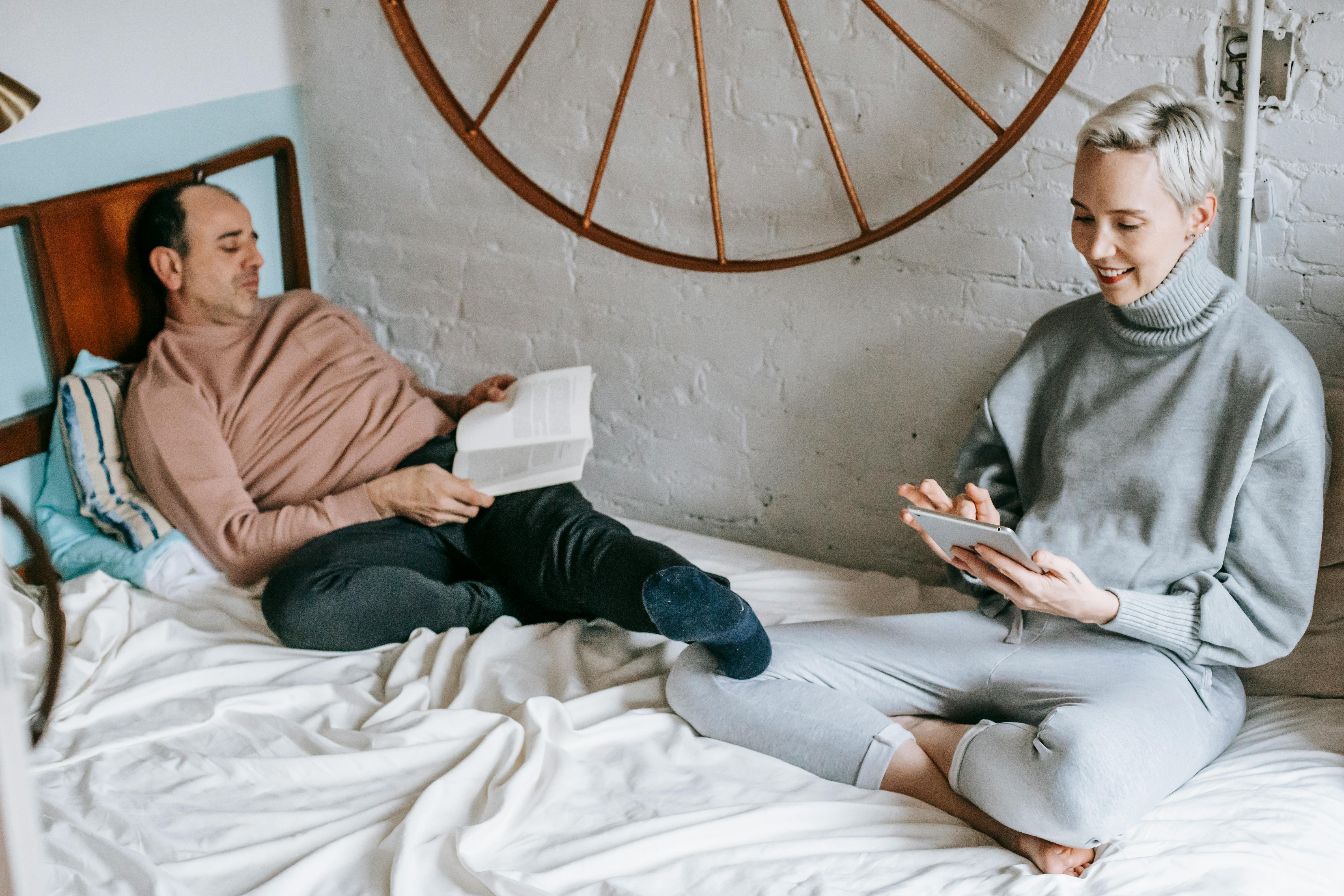 positive woman surfing tablet on bed near husband reading book