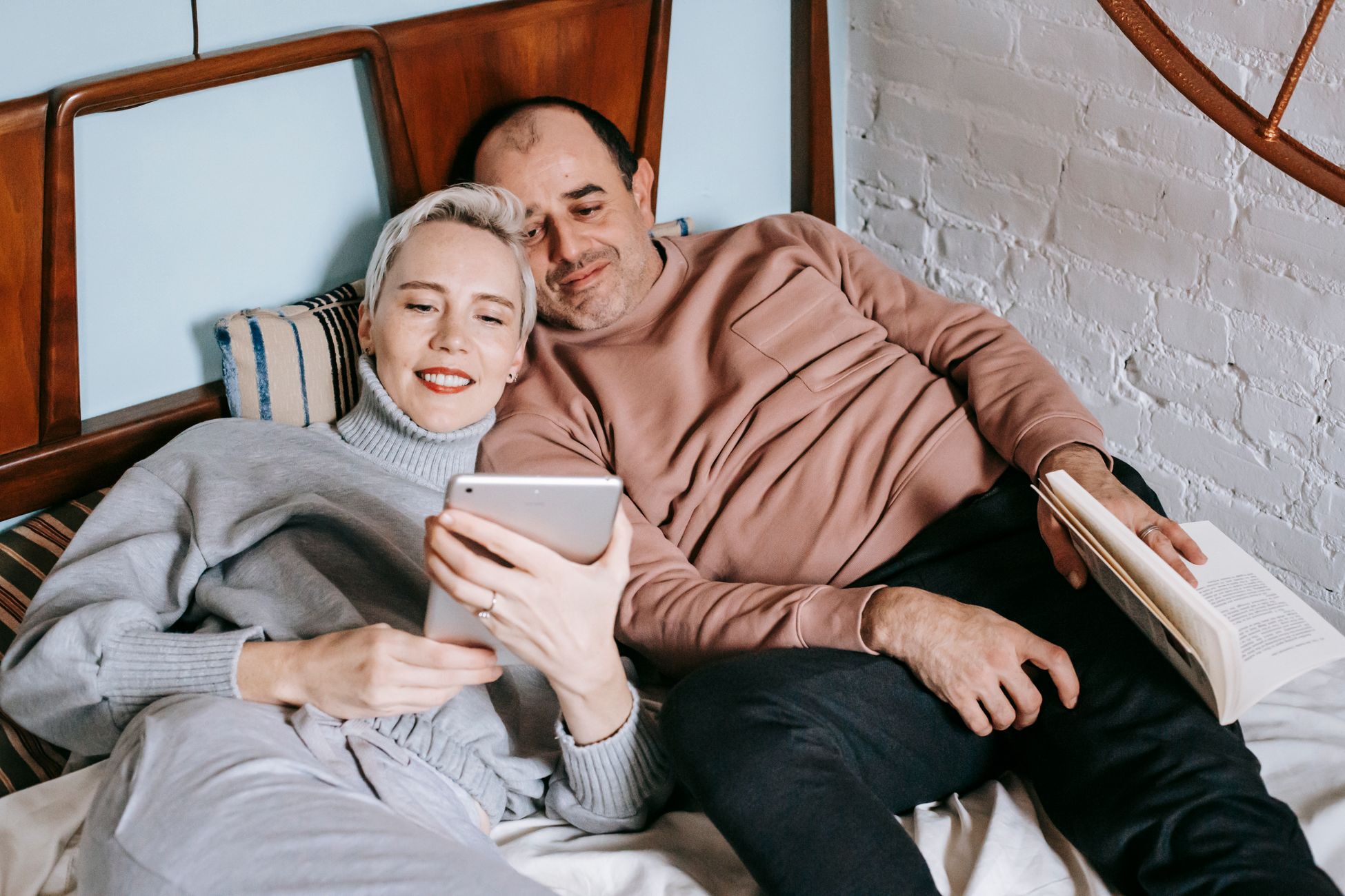 From above of happy adult diverse couple in casual outfits lying on bed and sharing table during weekend at home