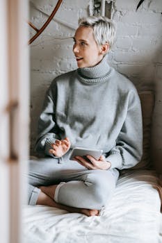 Woman relaxing in a cozy bedroom, holding a tablet and enjoying free time.