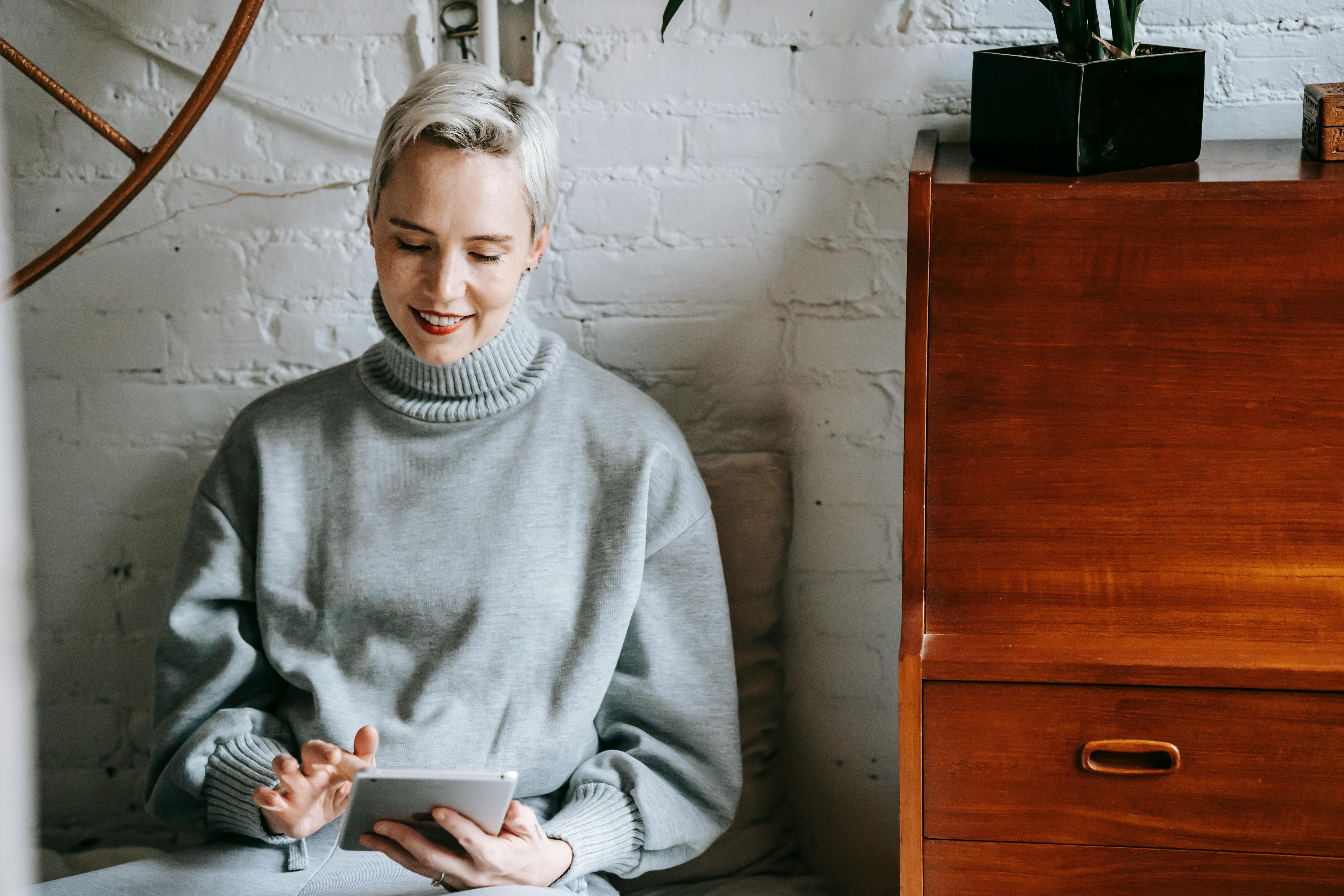 confident woman browsing tablet against white brick wall at home