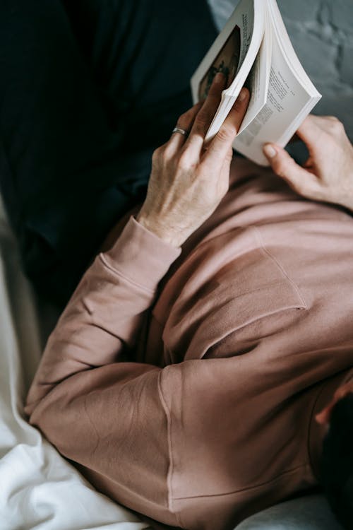 Faceless man reading book on bed during weekend at home