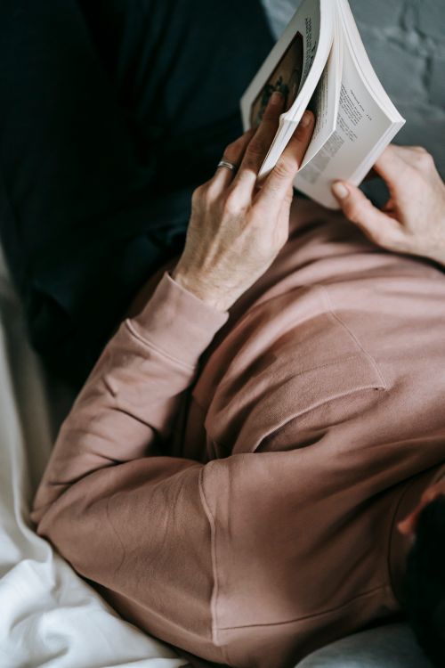 Free From above of crop unrecognizable male in casual clothes reading interesting novel while recreating on bed at home Stock Photo
