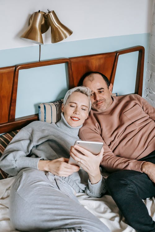 Delighted diverse couple lying on bed and sharing tablet