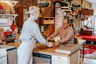 Adult glad man receiving cup of hot beverage from female partner at table in kitchen