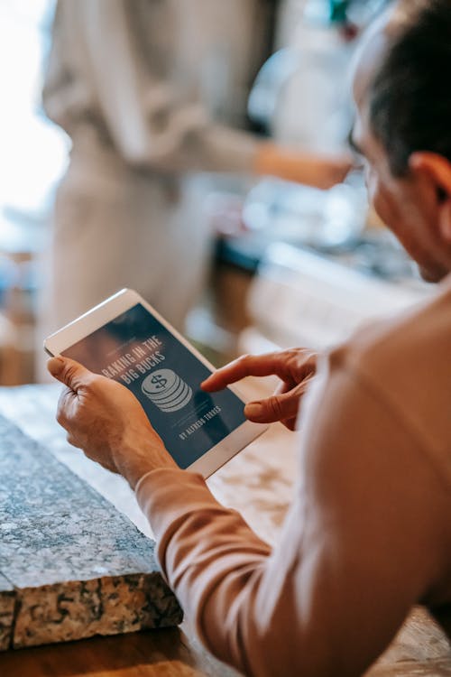 Free Anonymous man working remotely on tablet during breakfast with wife in kitchen Stock Photo