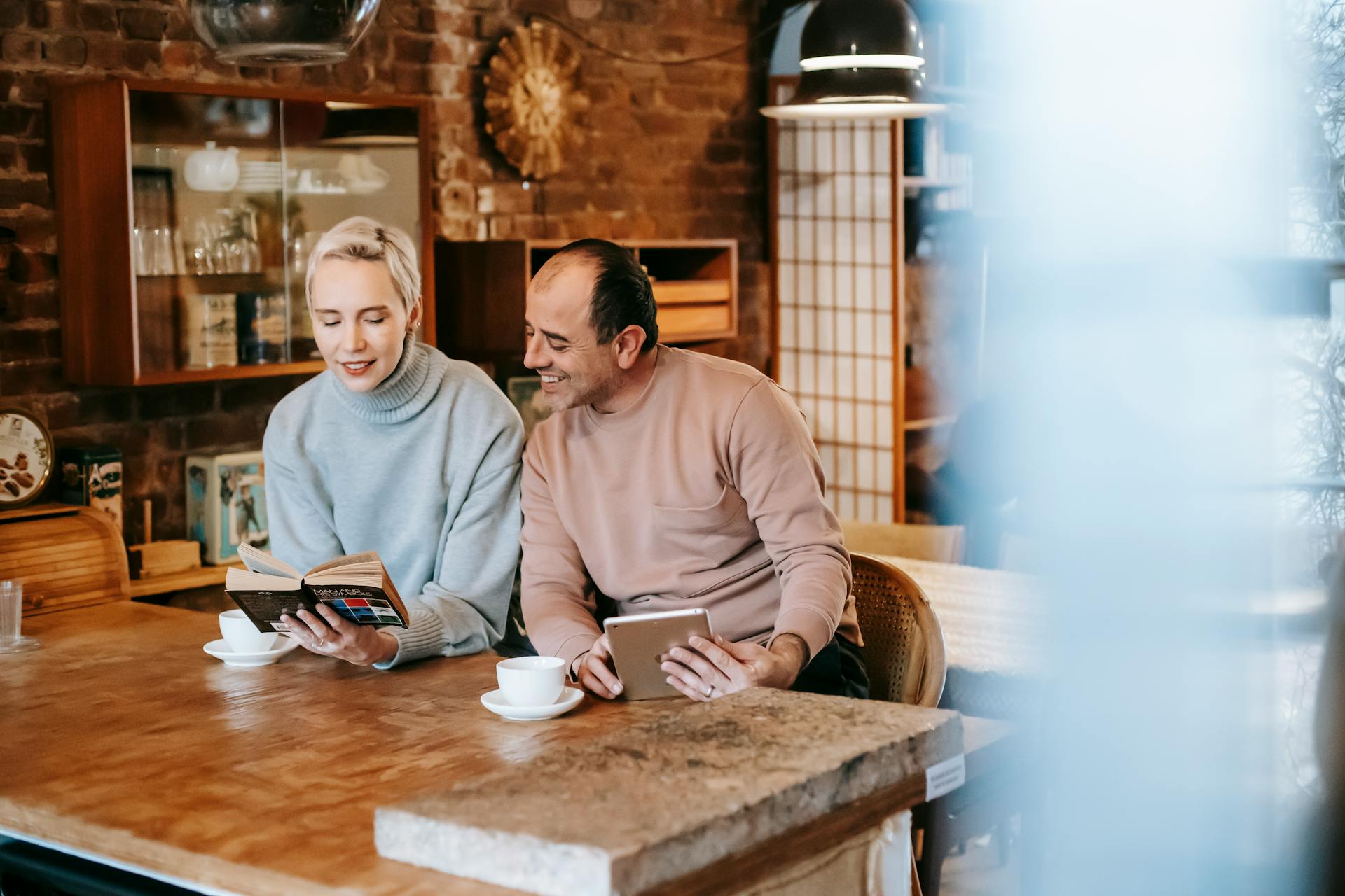 Woman reading book for ethnic husband browsing tablet at table