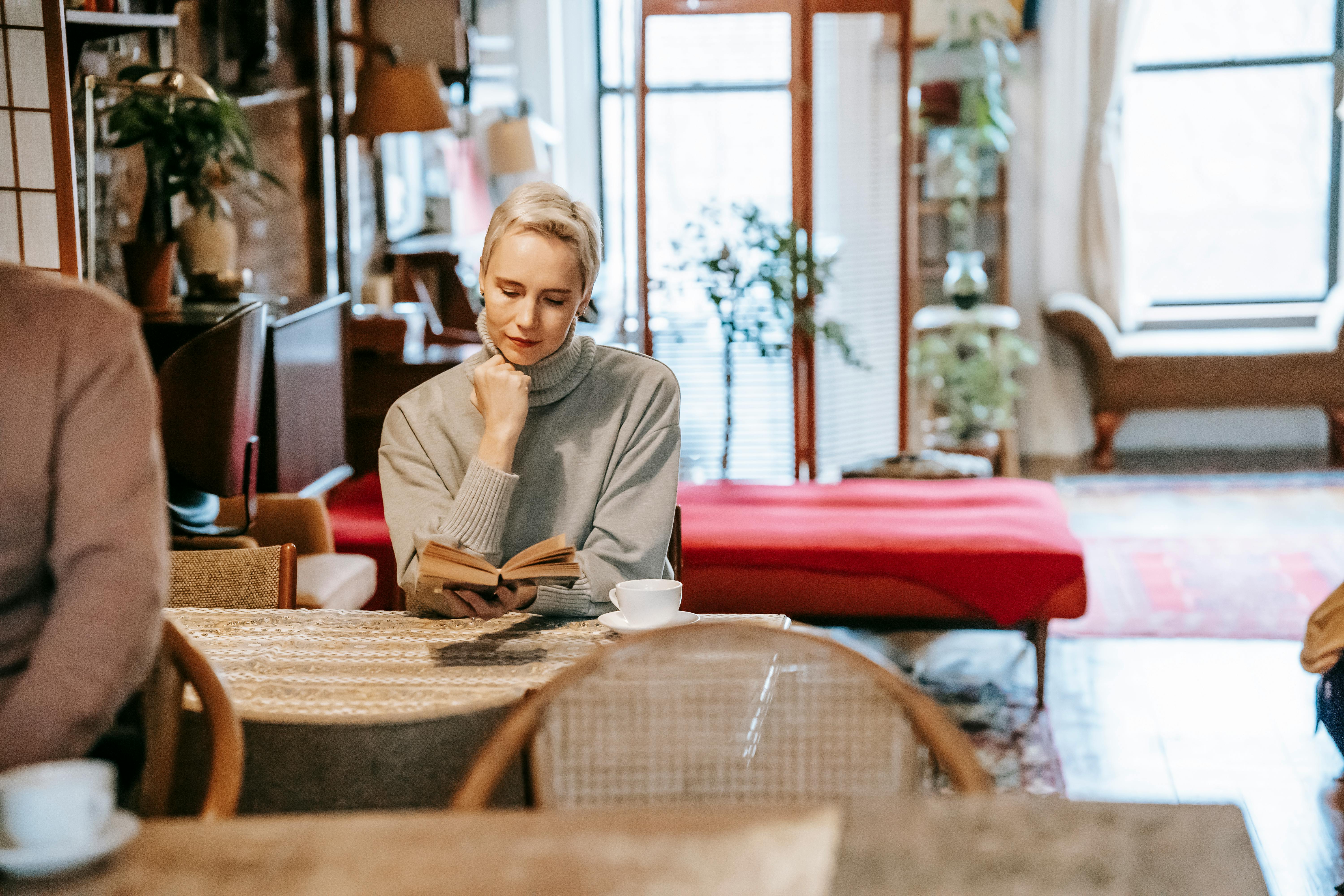 dreamy woman reading novel at table at home