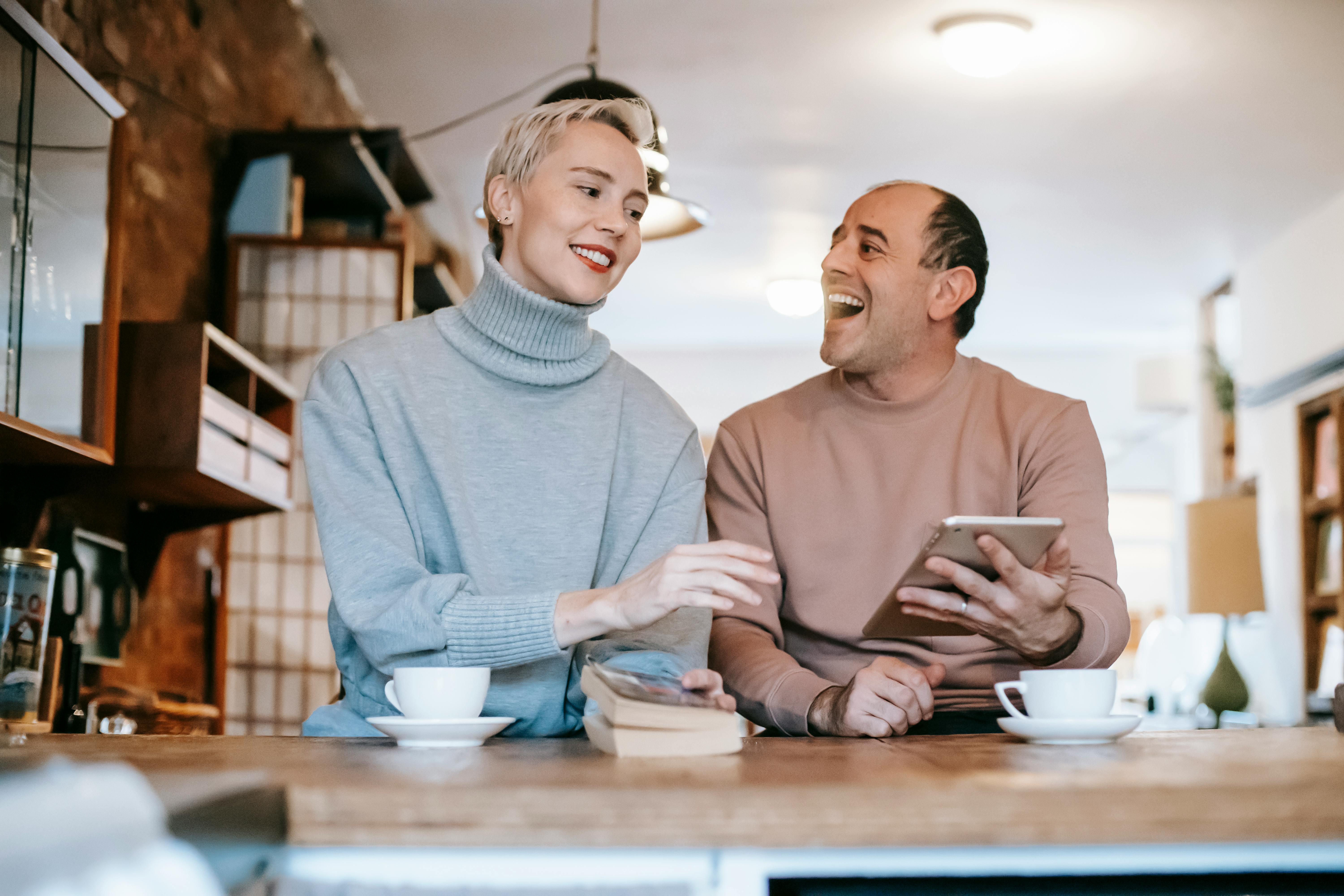 cheerful multiethnic spouses laughing while sharing tablet at table at home