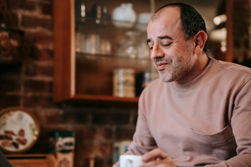 Content middle aged unshaven ethnic male in casual clothes reading coffee while resting at home during weekend