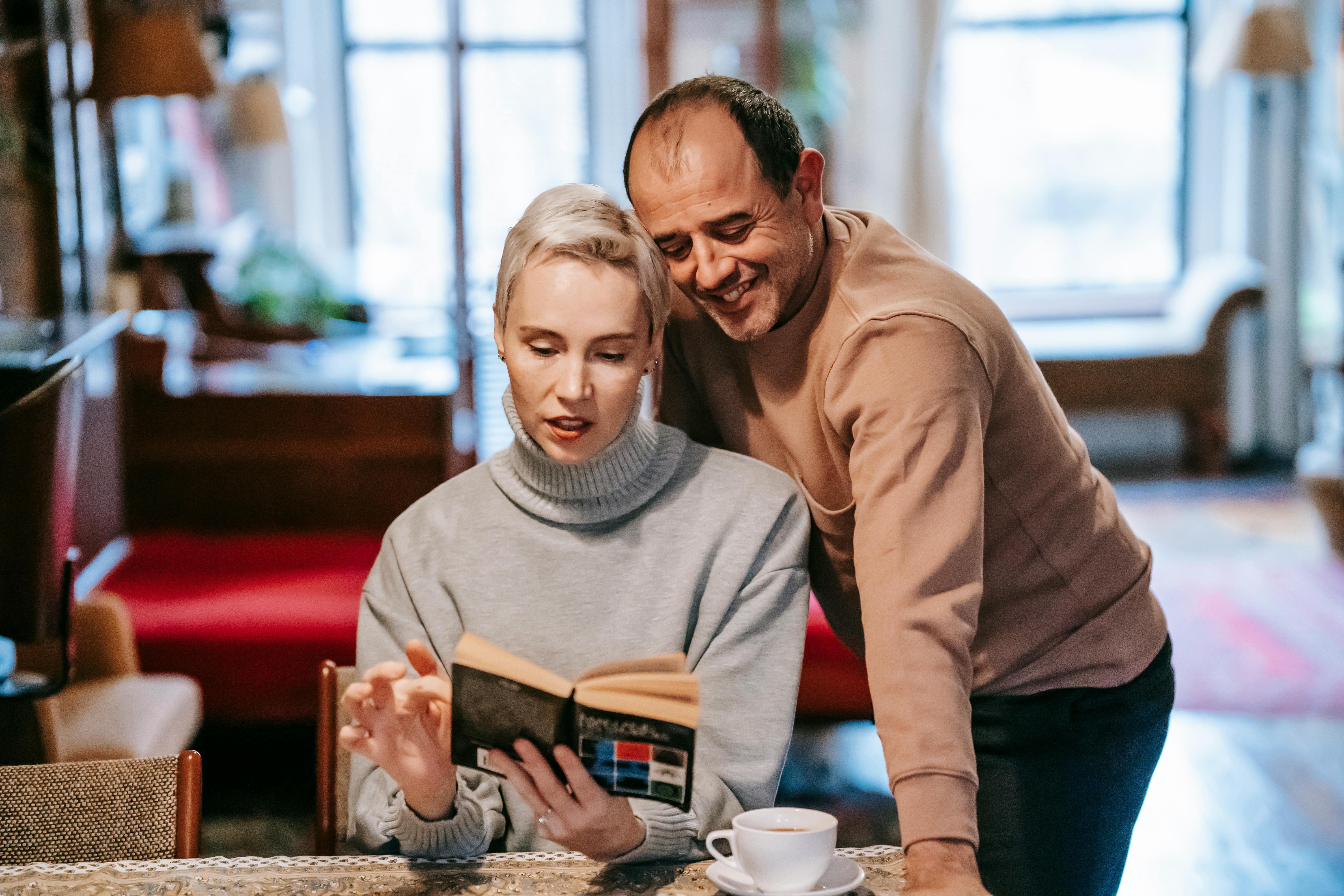 adult diverse couple reading interesting novel and drinking coffee at home