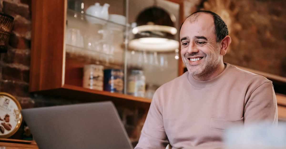 Person smiling while looking at a laptop in a warm home setting