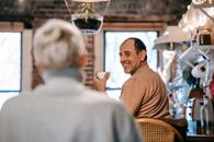 Back view of unrecognizable female in casual clothes speaking with happy middle aged ethnic husband drinking coffee at home
