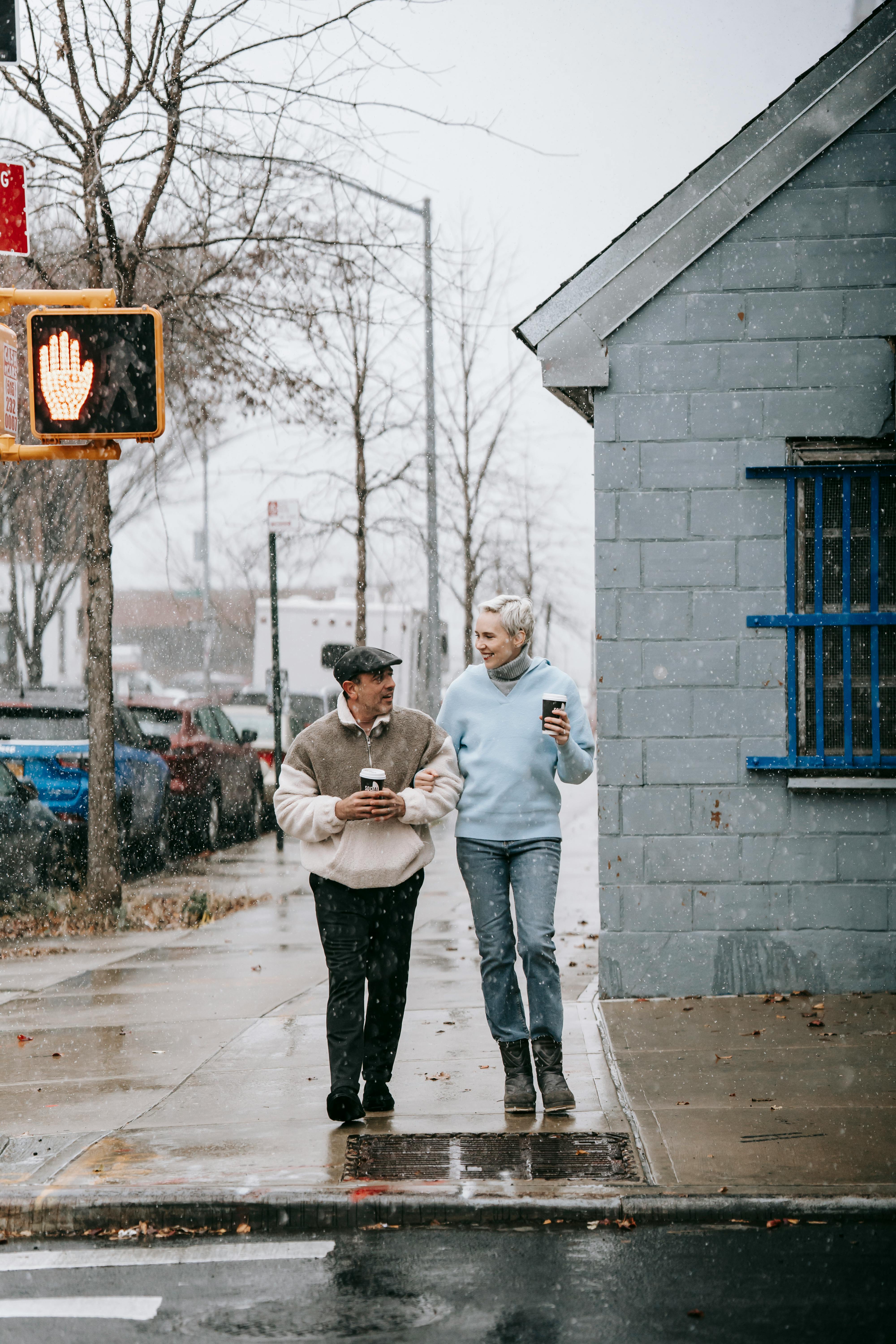 positive adult couple drinking takeaway beverage during walk in city