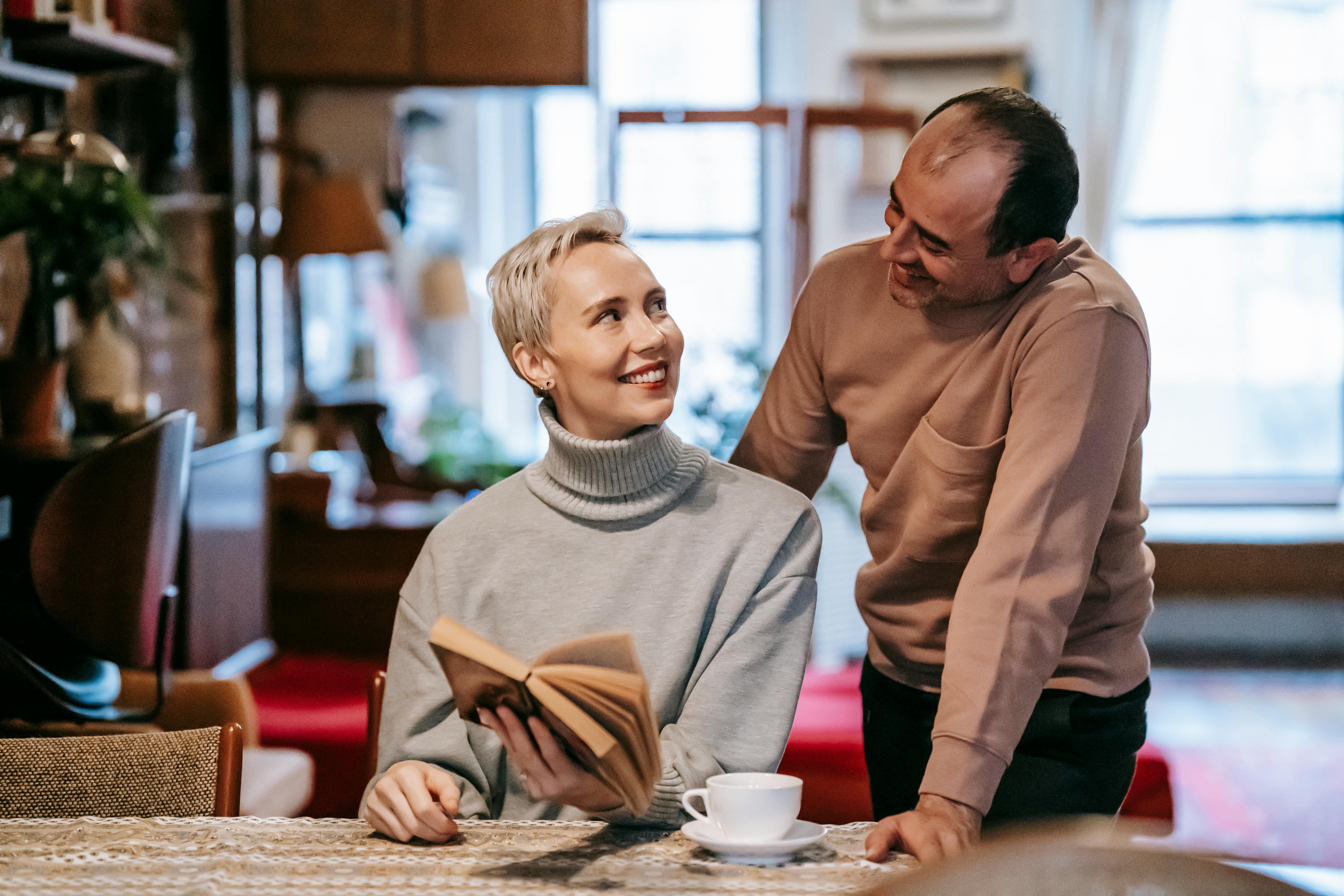 positive diverse spouses looking at each other while reading novel at home