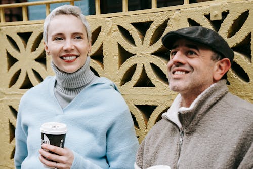 Smiling adult woman with takeaway hot beverage near friendly male beloved looking away on city street