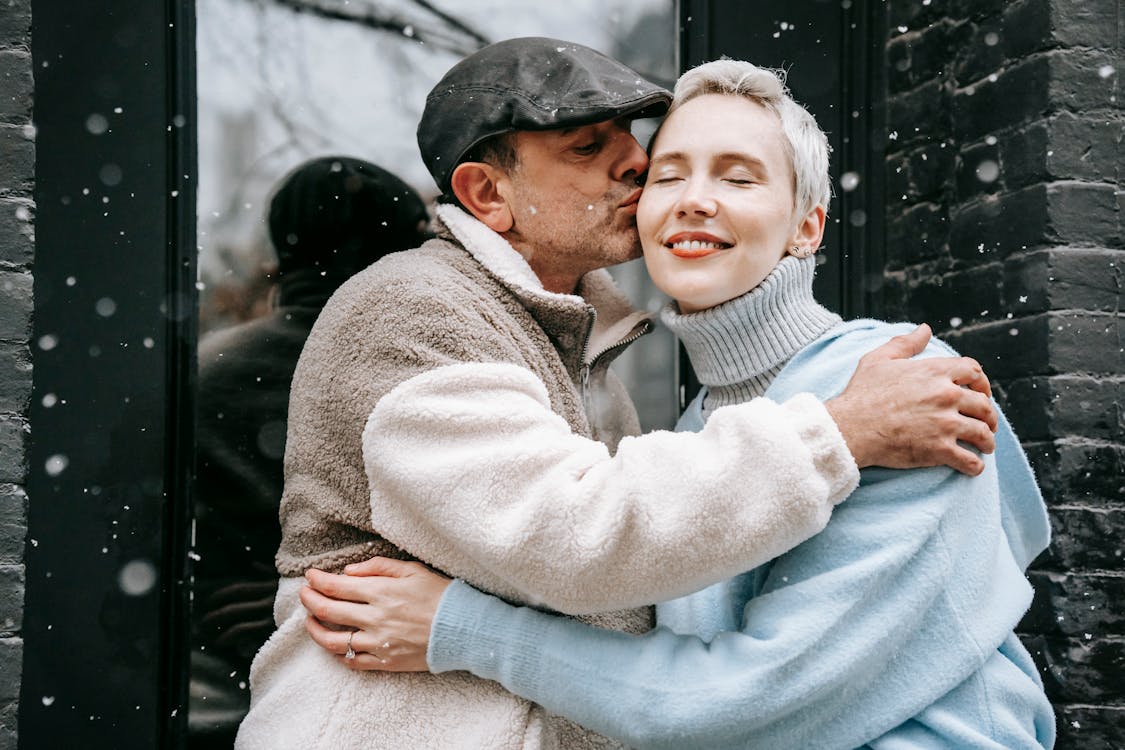 Free Man kissing dreamy girlfriend on city street in snowfall Stock Photo