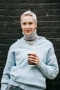 Smiling woman with takeaway coffee on street against brick wall