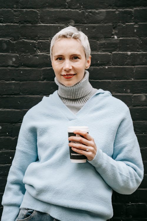 Free Smiling woman with takeaway coffee on street against brick wall Stock Photo