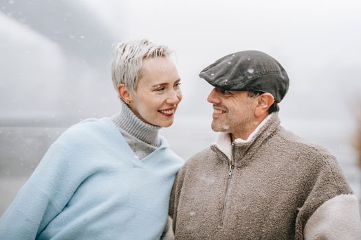 Smiling female in warm clothes talking to male beloved while looking at each other in town on foggy day