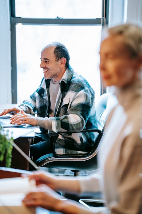 Cheerful coworkers smiling and speaking about job while working in contemporary office in daytime