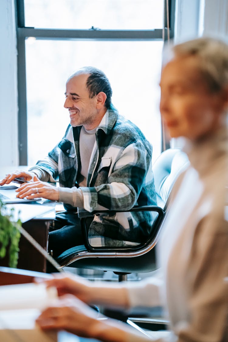 Positive Man And Woman Working Together At Tables In Office