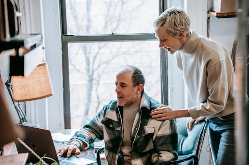 Cheerful woman helping colleague with laptop