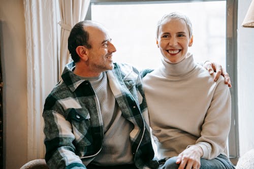Cheerful middle aged man hugging content smiling woman on window of lounge in daytime