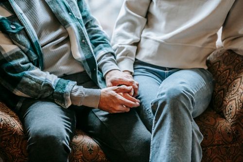 Free From above of crop anonymous couple in casual clothes holding hands on soft couch Stock Photo