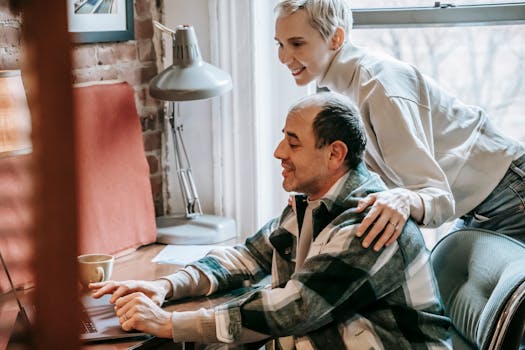 Crop happy woman with trendy short hairstyle embracing and watching man using netbook at table