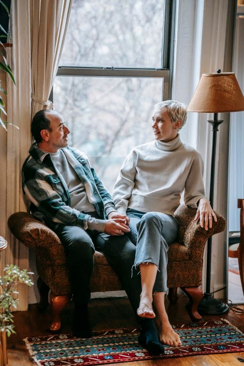 Free Full body of cheerful middle aged couple relaxing on couch while speaking in cozy lounge Stock Photo