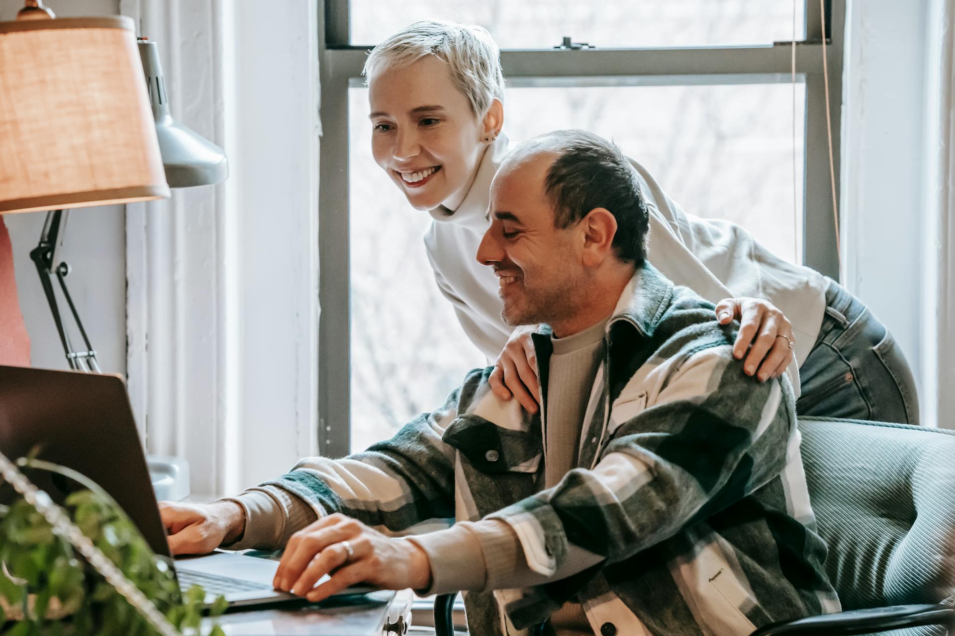 Smiling couple collaborating on a laptop indoors, fostering positive work environment.