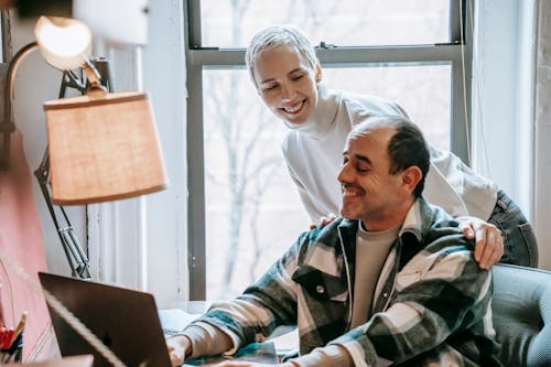 Happy middle aged couple smiling and talking about freelance project at netbook near lamp on table