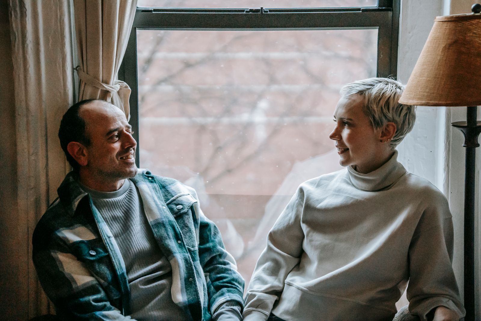 Two adults seated together beside a window