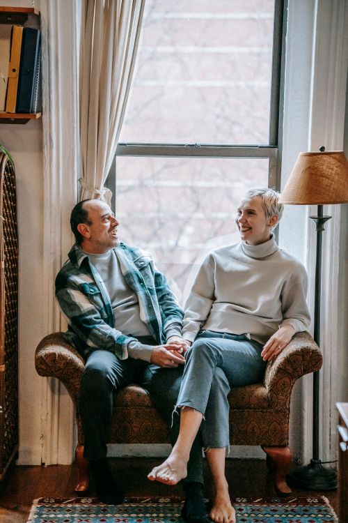 Free Full body of cheerful middle aged couple smiling and talking near window in cozy living room Stock Photo