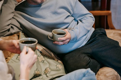 Free Crop anonymous couple with mugs of tasty aromatic strong coffee on sofa in lounge Stock Photo