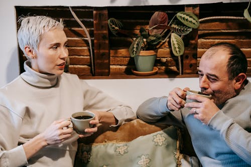 Free Calm multiracial friends in casual clothes drinking cups of coffee and communicating while spending time in cafe Stock Photo