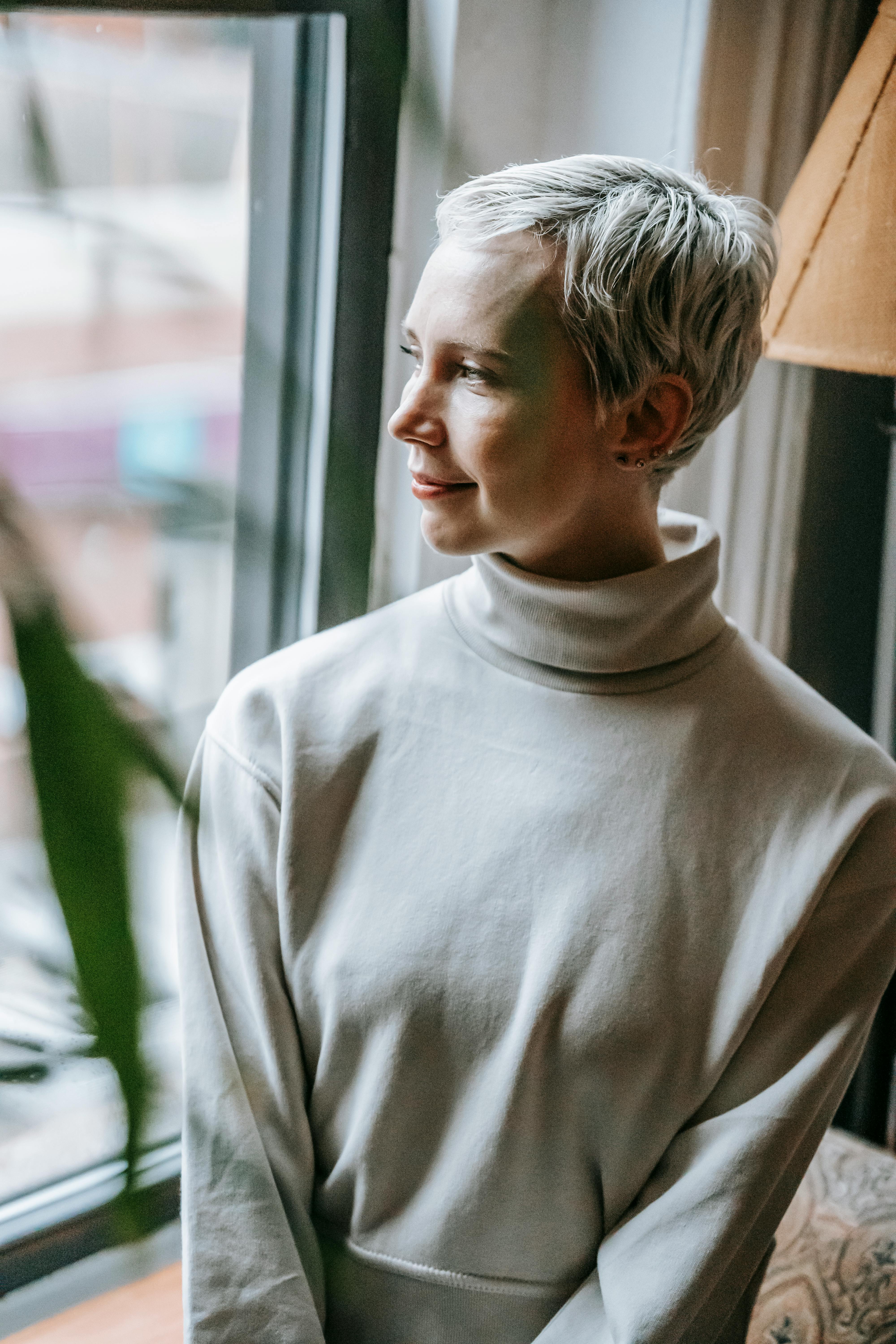 thoughtful woman looking away near window and plant in apartment