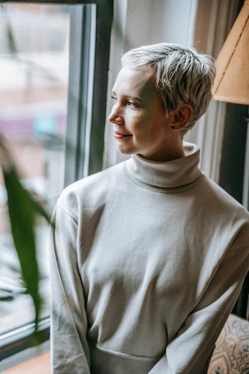 Wanita Dengan Sweater Turtleneck Putih Berdiri Dekat Jendela Kaca