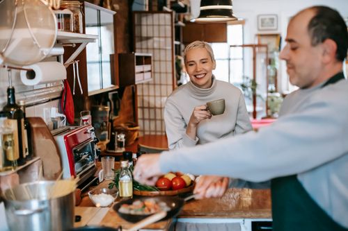Free Male seasoning delicious meatballs in pan against cheerful female beloved with cup of coffee in kitchen Stock Photo