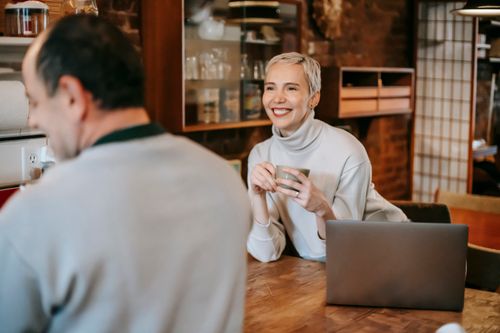 Free Cheerful female with cup of hot beverage against laptop speaking with male beloved in house Stock Photo