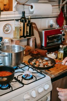 Crop unrecognizable person with tasty meatballs in pan against gas stove with saucepans during cooking process at home — photo by Gary  Barnes