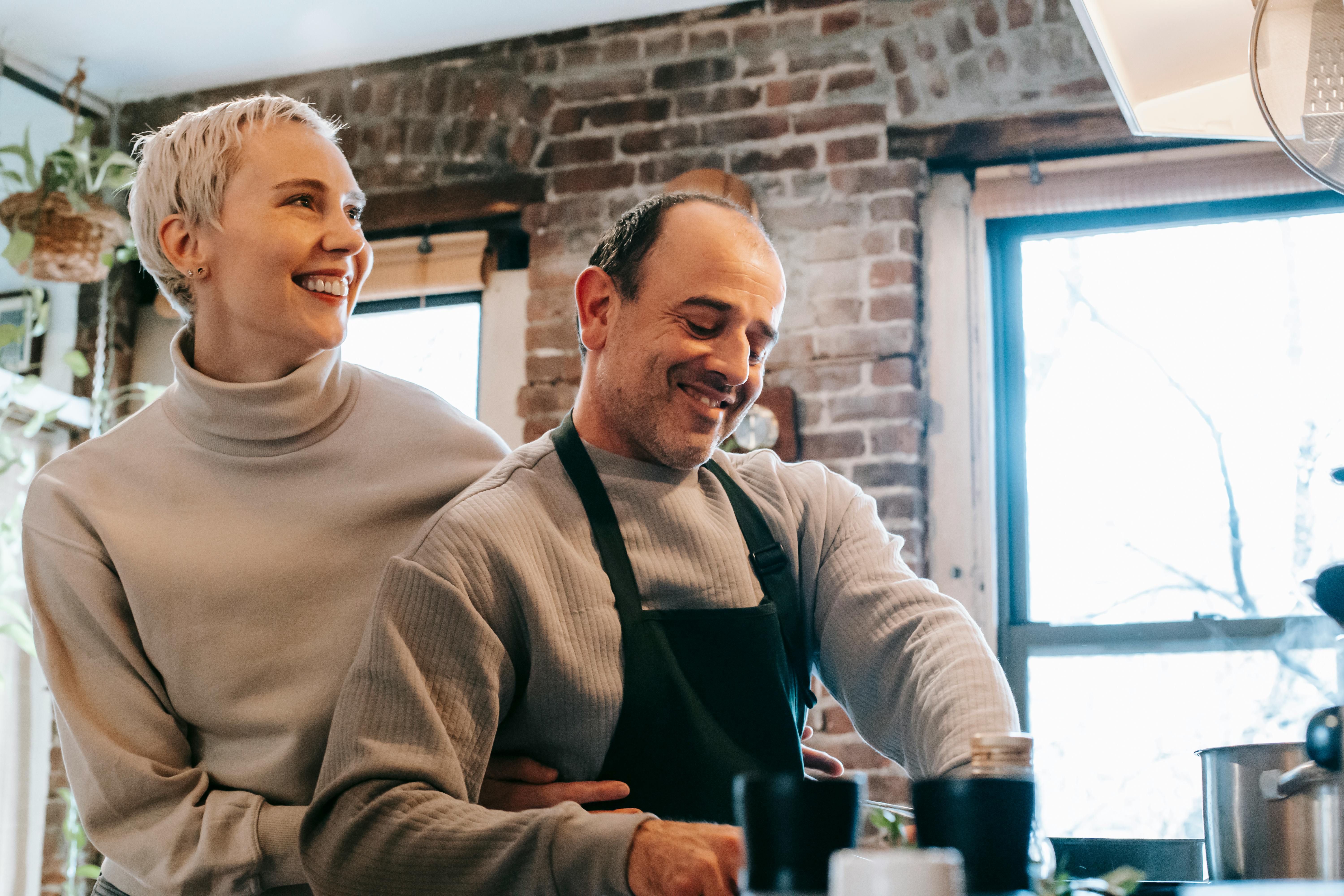 A cheerful couple bonding while preparing food in their rustic kitchen.