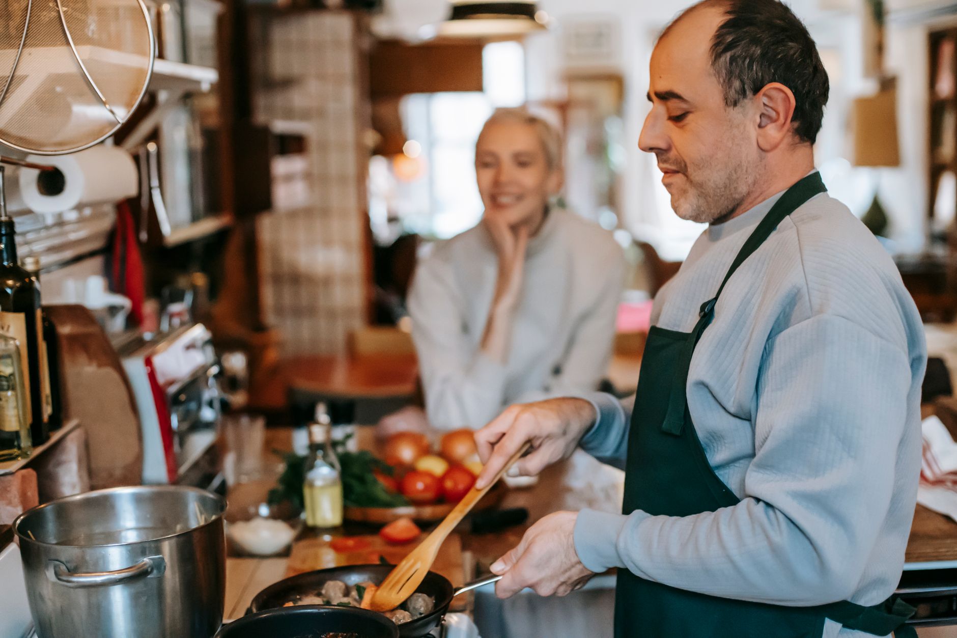 Crop male stirring tasty meatballs in pan while preparing lunch against smiling female beloved at home