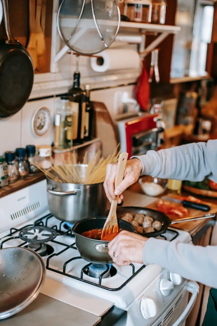 Crop Person Stirring Tomato Sauce Against Meatballs In Kitchen