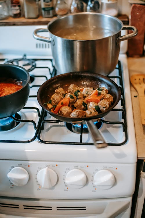 Pan with saucy meatballs frying on gas stove in kitchen