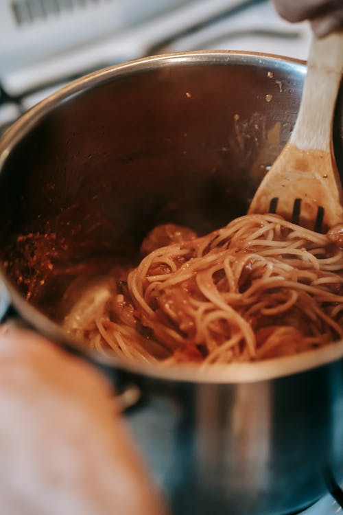 Free From above of appetizing homemade spaghetti with tomato sauce and meatballs in metal saucepan placed on stove in kitchen Stock Photo