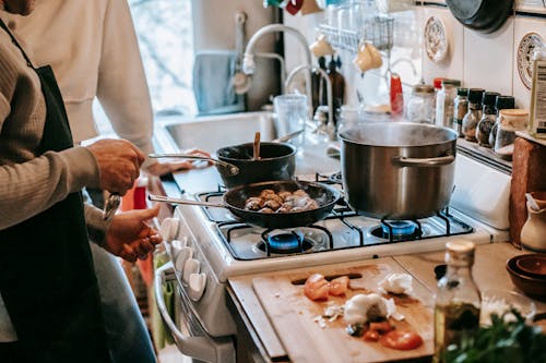 Anonymous man frying meatballs standing in kitchen with wife